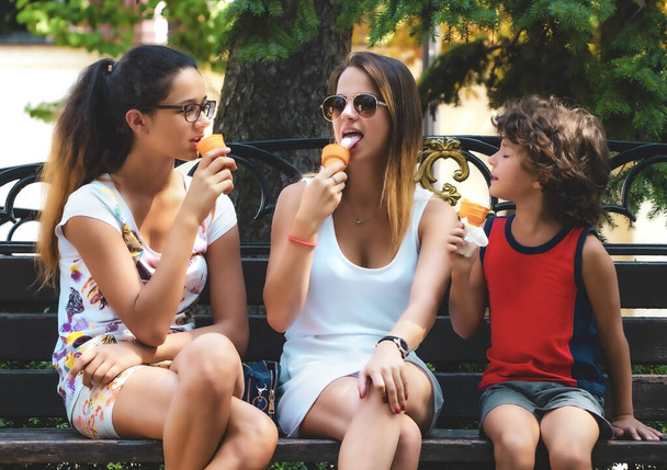 Happy family eating ice cream in a summer park. Sisters and little brother have fun. Walk in the green park - Zdjęcie, obraz