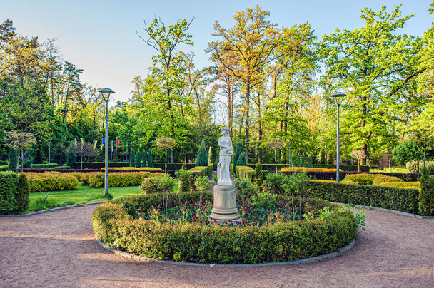 гіпсова скульптура жінки з глечиком на квітці серед кущів і дерев у міському парку в Бучі (Україна). - Фото, зображення