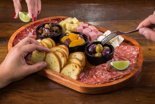 People eating wooden cutting board with cheese, cold cuts and jams. - Photo, Image