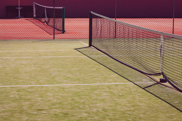 Canchas de tenis, de color verde y rojo. Red de tenis en perspectiva. Nadie en la foto
. - Foto, Imagen