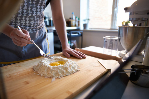 Nimetön henkilö tekee tuoretta pastaa kotona keittiössä, katselee videoreseptiä munien ja jauhojen kanssa. - Valokuva, kuva