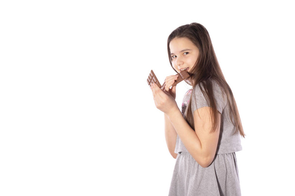 girl with black hair bites a bar of chocolate and hides on a white background - Foto, Bild