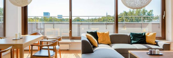 Panorama of elegant living room with wooden dining table, corner sofa with coffee table and big window doors to terrace around room - Fotoğraf, Görsel