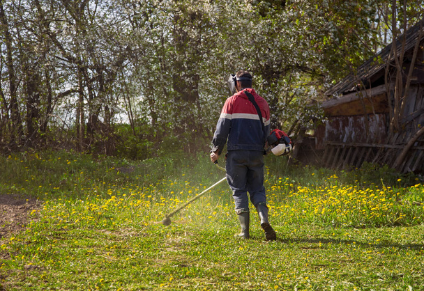 Nuori mies leikkaa ruohoa trimmerillä kesällä
 - Valokuva, kuva