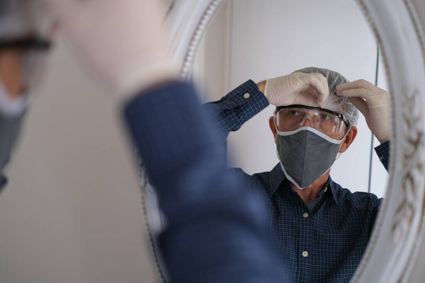Homem de meia-idade usa máscara higiênica para evitar infecções doenças respiratórias transmitidas pelo ar, como infecção, gripe, 2019-nCoV na frente do espelho para sair
. - Foto, Imagem