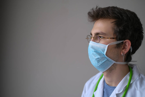 Portrait of the handsome young doctor. He is standing front of the gray background. - Foto, Imagen