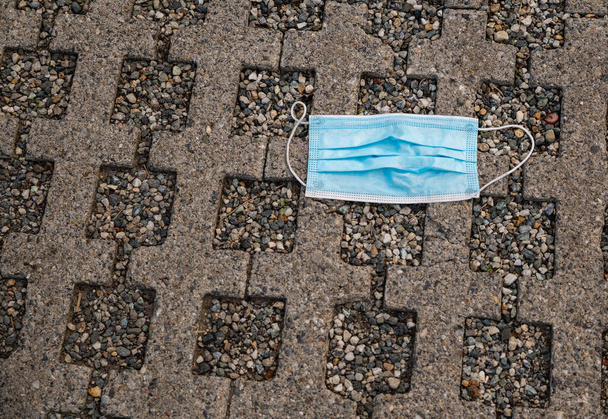 The coronavirus pandemic did not change the bad habits: a disposable blue surgical mask was irresponsibly thrown on the ground in a parking lot at a shopping center. - Photo, Image