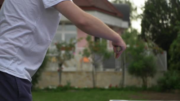 男は庭で卓球をする。プレイヤーは屋外ピンポンゲームでボールを打つ - 映像、動画