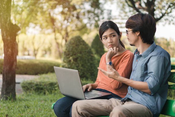 Young business asian man and woman working with them laptop and look at the face together on a bench in the park outdoors on vacation time. - Zdjęcie, obraz