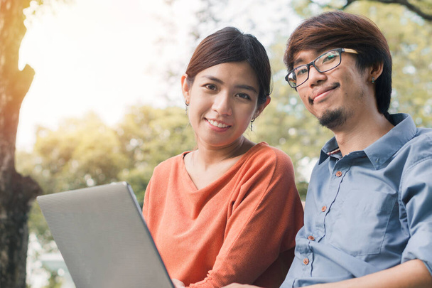 Couple young asian man and woman working with laptop and enjoying cheerful his online winner success  on a bench in the park outdoors on vacation time. - Zdjęcie, obraz