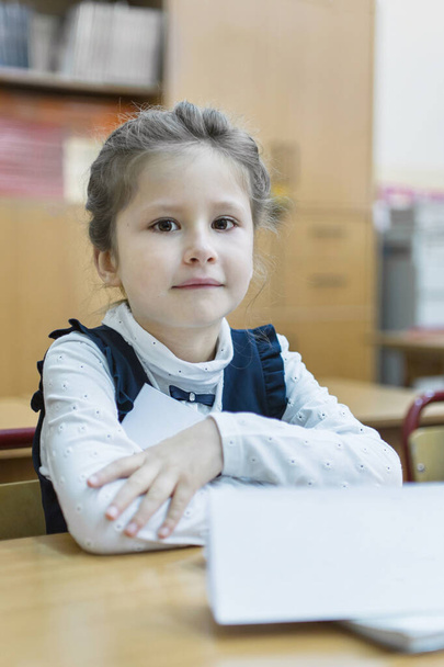 A schoolgirl of primary classes sits at a desk. Hands folded on top of each other and she listens to a lesson. Day of knowledge. First of September. The beginning of the school year. Concept of education. - Foto, Bild
