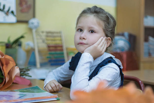 A thoughtful schoolgirl of primary classes sits at a desk and listens to a lesson. Day of knowledge. First of September. The beginning of the school year. Concept of education. - Fotoğraf, Görsel