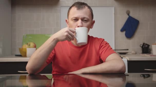Atrakcyjny młodzieniec pije z białego kubka - Materiał filmowy, wideo