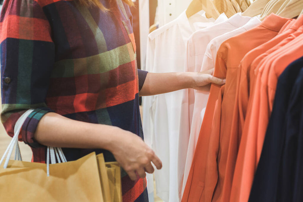 Молодая азиатская женщина с сумками выбор одежды в торговом центре или магазине одежды, Селективный фокус
. - Фото, изображение