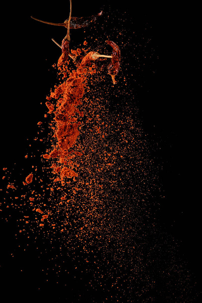 Red paprika spices powder explosion, flying chili pepper isolated on black background. Splash of spice background.  - Foto, Imagem