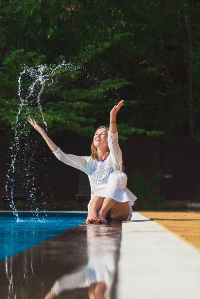 молода жінка бризкається під час сидіння біля басейну
 - Фото, зображення