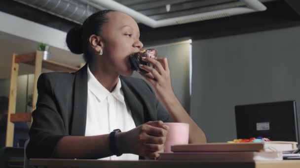 Down view of african american woman having lunch at office. Woman eats muffin and drinks a coffee - Video
