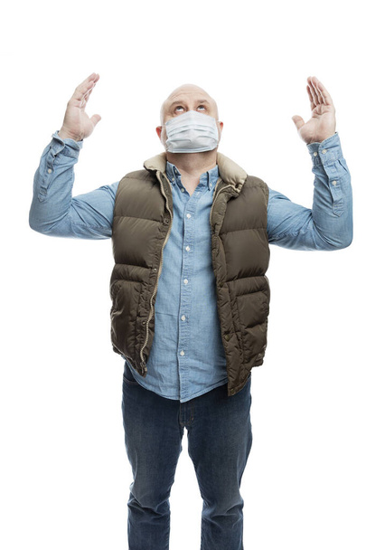 Adult bald man in a medical mask raised his hands up in prayer. The financial crisis and quarantine during the coronavirus pandemic. Precautionary measures. Isolated on a white background. Vertical. - Foto, afbeelding