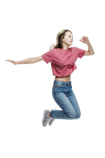 A smiling young girl in jeans and a red T-shirt is jumping. Positive and happy. Eared on a white background. Full height. Vertical. - Zdjęcie, obraz