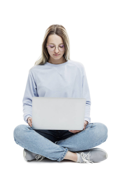 Uśmiechnięta młoda dziewczyna w okularach siedzi z laptopem w rękach. Edukacja, praca i blogi. Odizolowany na białym tle. Pionowe. - Zdjęcie, obraz