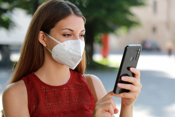 COVID-19 Close Up Young Woman Wearing KN95 FFP2 Mask Using Smart Phone App in City Street to Aid Contact Tracing and Self Diagnostic in response to Coronavirus Disease 2019 - Fotografie, Obrázek