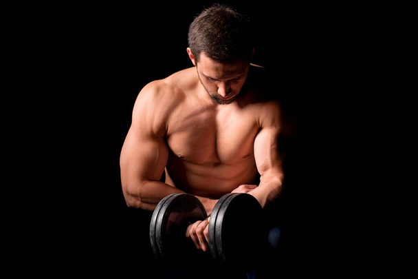 筋肉の体を持つ強い男が働いている。黒の背景にダンベルと体重運動. - 写真・画像