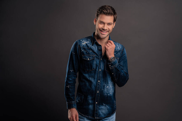 Confident and handsome. Handsome young man in denim shirt looking at camera and smiling while standing against grey background. - Photo, Image