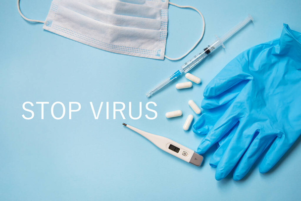青い背景にある青いラテックス手袋は、薬、医療用マスク、温度計、注射器が付いています。ウイルスや流行のための健康と自己制御の概念。碑文停止ウイルス. - 写真・画像