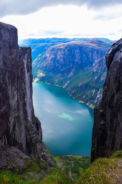 Вид на Люсе-фьорд через трещину между двумя скалами высотой 984 метра, где рядом застрял знаменитый Керагболтен - самый опасный камень в мире. Горный Кьераг, графство Рогаланд, Норвегия
. - Фото, изображение