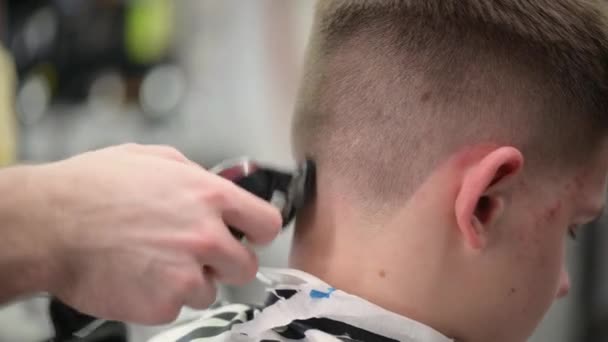 Haarschnitt des jungen Mannes im Friseurladen. Nahaufnahme des Haarschneidemeisters mit Haarschneidemaschine am Hinterkopf - Filmmaterial, Video
