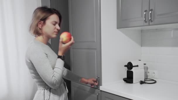 Женщина открывает дверь холодильника на кухне дома, берет яблоко затем кладет его обратно и берет пончик
 - Кадры, видео