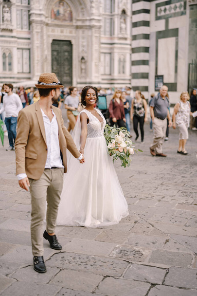 Pareja de boda interracial. Boda en Florencia, Italia. Novia afroamericana y novio caucásico caminata por la Piazza del Duomo
. - Foto, imagen
