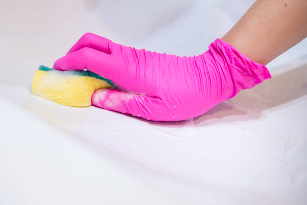 A hand in a pink glove washes a washbasin in the bathroom with a sponge with foaming detergent. Cleaning company cleans the house. Disinfection of the senile node from viruses and bacteria. - Fotografie, Obrázek