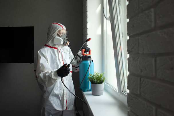 Controlo de pragas. Um trabalhador em um terno protetor limpa o quarto de baratas e ratos com uma pistola de pulverização, o serviço sanitário desinfecta o apartamento com um agente químico
 - Foto, Imagem