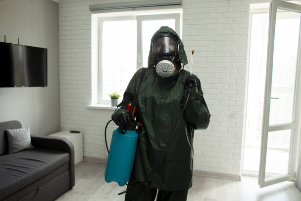 Controlo de pragas. Trabalhador em um terno de proteção contra o fundo de um apartamento com um spray, o serviço sanitário desinfecta o quarto com um agente químico
 - Foto, Imagem