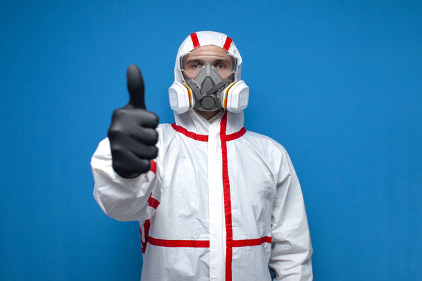 epidemiologist in a chemical protective suit shows an like sign on a blue isolated background, man, biologist, scientist, virologist. Everything's under control - Fotografie, Obrázek