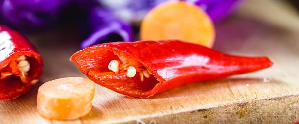 Rode peper en gehakte groenten, gesneden op houten tafel, keukeningrediënten gebruikt in veganistisch voedsel. - Foto, afbeelding