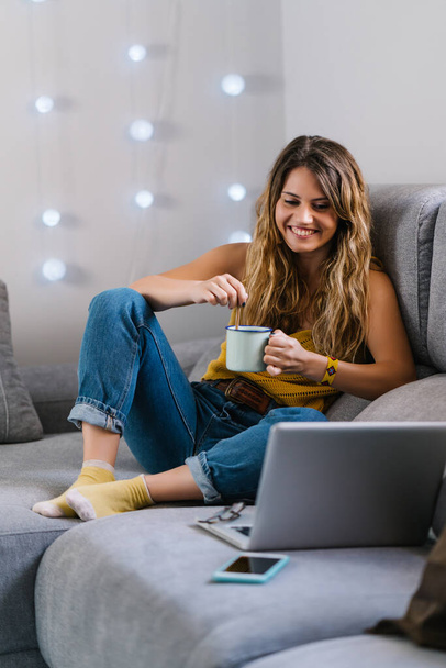 Žena sedí na pohovce pomocí notebooku a pije kávu - Fotografie, Obrázek