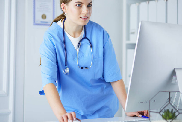 Portrait of female physician filling up medical form while standing near reception desk at clinic or emergency hospital - Photo, image