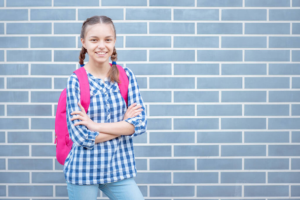 Beautiful student teenager schoolchild with backpack looking at camera. Smiling cute child with bag. Teen girl with braided hair against a brick wall outdoors. Childhood and Back to school concept. - Fotó, kép