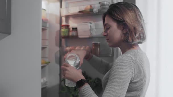 Κοντινό πλάνο της γυναίκας ανοίγει πόρτα ψυγείο στην κουζίνα στο σπίτι και παίρνει ένα μπουκάλι γάλα, τότε ρίχνει γάλα σε γυαλί - Πλάνα, βίντεο