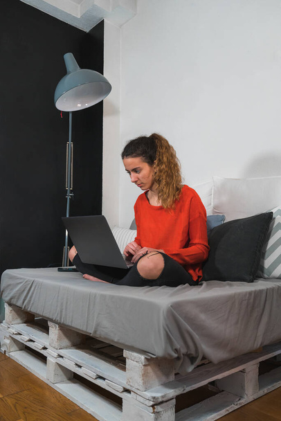 Un joven estudiante usando el ordenador sentado en el sofá. Adolescente estudiando en su habitación. Trabajo remoto. Trabajando remotamente desde casa. Adolescente usando el portátil en casa
. - Foto, Imagen