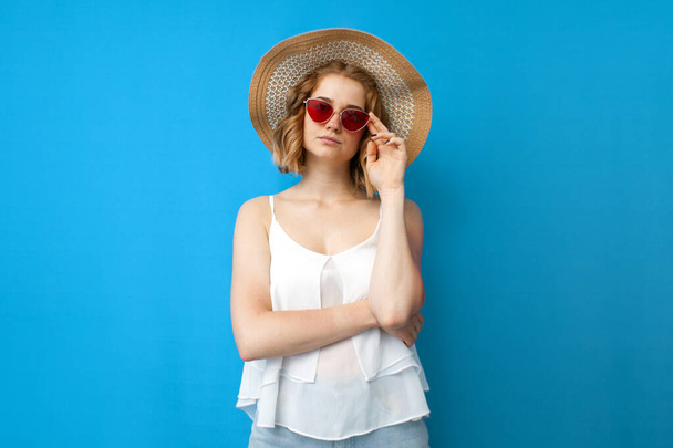 летняя концепция. молодая серьезная девушка в шляпе и очках на голубом изолированном фоне, женщина в летней одежде на отдыхе
 - Фото, изображение