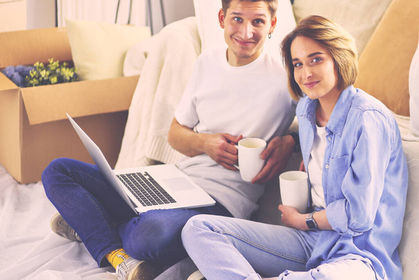 Couple buying online with a laptop and moving house sitting on the floor - Zdjęcie, obraz