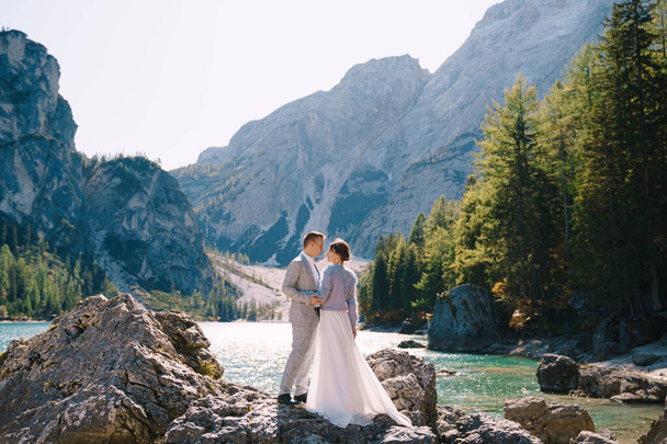 Gelin ve damat İtalya 'daki Lago di Braies' e bakan taşların üzerinde duruyorlar. Düğün Avrupa 'da, Braies Gölü' nde. Sevgi dolu yeni evliler inanılmaz doğanın arka planında yürür.. - Fotoğraf, Görsel