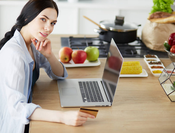 Usmívající se žena on-line nakupování pomocí počítače a kreditní karty v kuchyni - Fotografie, Obrázek
