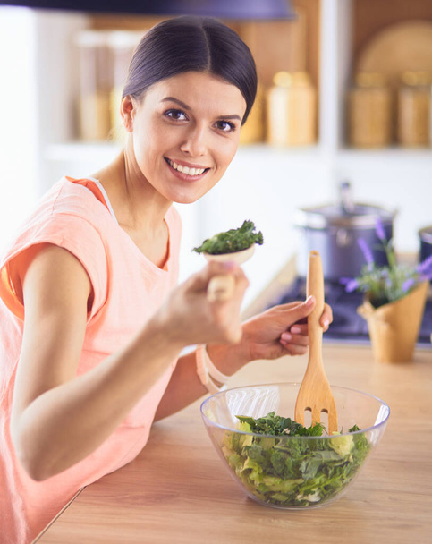 Smiling young woman mixing fresh salad in the kitchen. - Photo, image