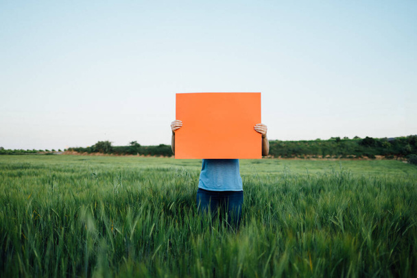 κορίτσι που κρατά μια πορτοκαλί πινακίδα σε ένα πράσινο πεδίο - Φωτογραφία, εικόνα