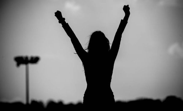 Ασπρόμαυρη φωτογραφία. Η σιλουέτα ενός κοριτσιού με σηκωμένα χέρια στο γήπεδο ποδοσφαίρου. Νίκη - Φωτογραφία, εικόνα