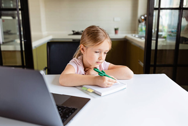 Pretty schoolgirl studying homework during her online lesson at home, social distance during quarantine covid-19, self-isolation, online education concept, home schooler. Workplace in living room - Foto, Imagen